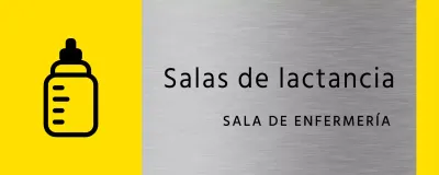 Sencilla señalización en amarillo y negro con el nombre de la sala de lactancia del edificio y un icono cuadrado de un biberón.